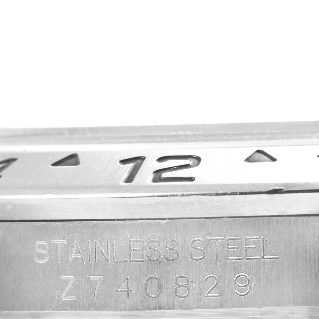 This close-up image of a Rolex Explorer 16570 Men's Stainless Steel Black Dial 16570 Men's Stainless Steel Black Dial watch shows part of the bezel with the number 12 and the serial number engraving.