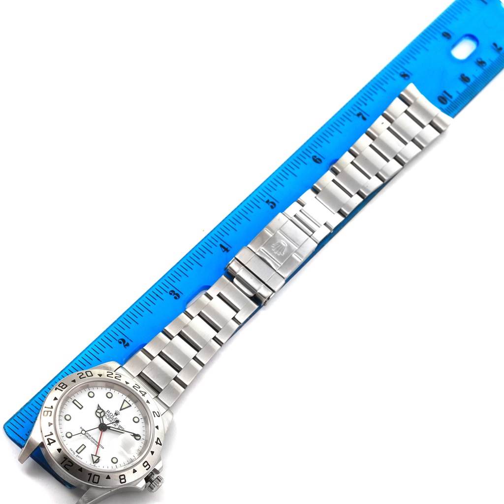 The image shows a Rolex Explorer 16570 Men's Stainless Steel White Dial 16570 Men's Stainless Steel White Dial watch laid flat, with a blue ruler measuring its length from the top of the watch case to the clasp.