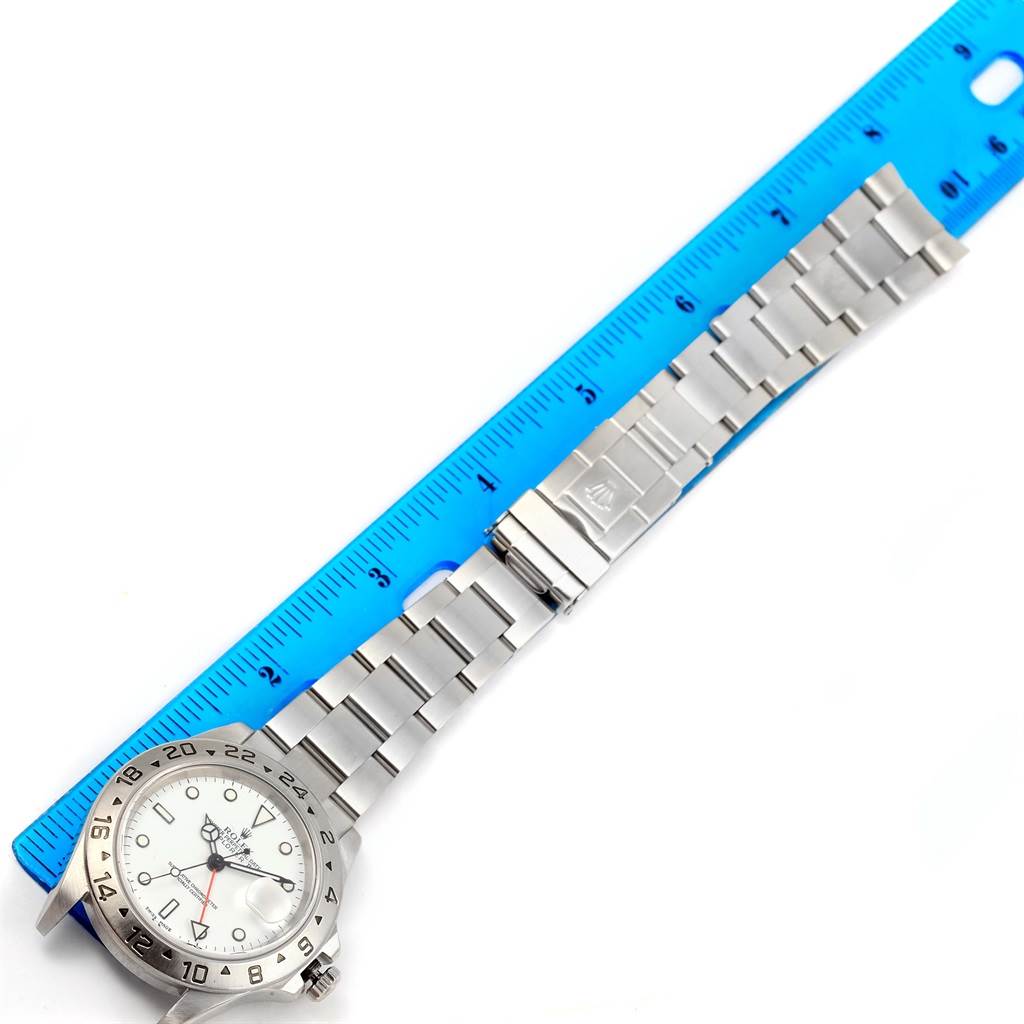 The Rolex Explorer 16570 Men's Stainless Steel White Dial 16570 Men's Stainless Steel White Dial watch is positioned flat, showing the dial, bezel, bracelet, and clasp alongside a blue ruler.