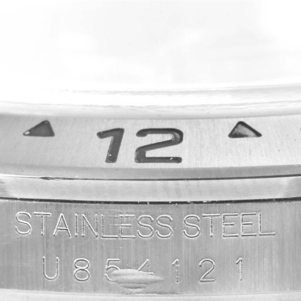 The image shows a close-up of the bezel and case back engraving on a Rolex Explorer 16570 Men's Stainless Steel Black Dial 16570 Men's Stainless Steel Black Dial model watch, showcasing "12," "STAINLESS STEEL," and a serial number.