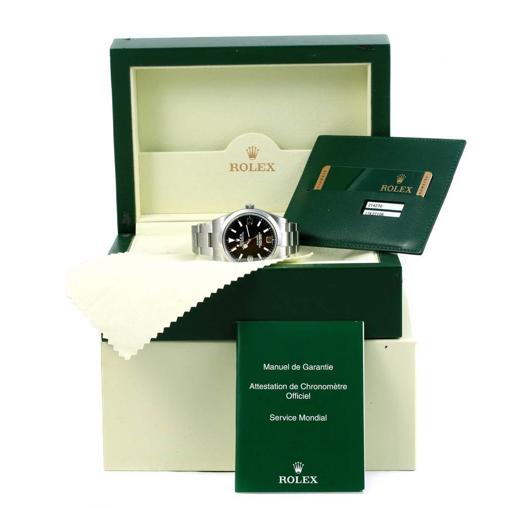 The Rolex Explorer 214270 Men's Stainless Steel Black Dial 214270 Men's Stainless Steel Black Dial watch is shown from a front angle, nestled in its open box with accompanying warranty and service documents.