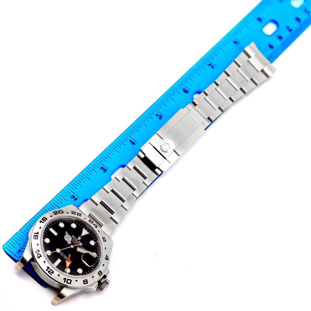 The Rolex Explorer 216570 Men's Stainless Steel Black Dial 216570 Men's Stainless Steel Black Dial watch is shown flat with the face, bezel, and full bracelet displayed alongside a blue ruler.