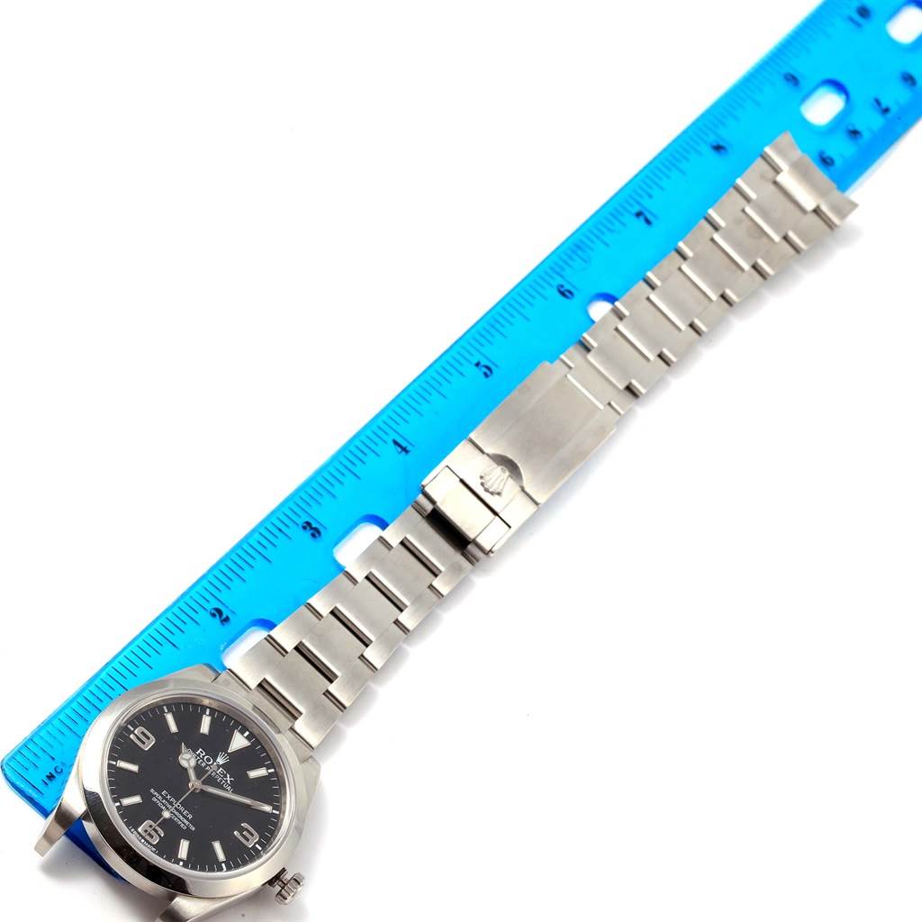 The image shows a Rolex Explorer 214270 Men's Stainless Steel Black Dial 214270 Men's Stainless Steel Black Dial watch laid flat with a blue ruler, displaying the face and stainless steel bracelet.