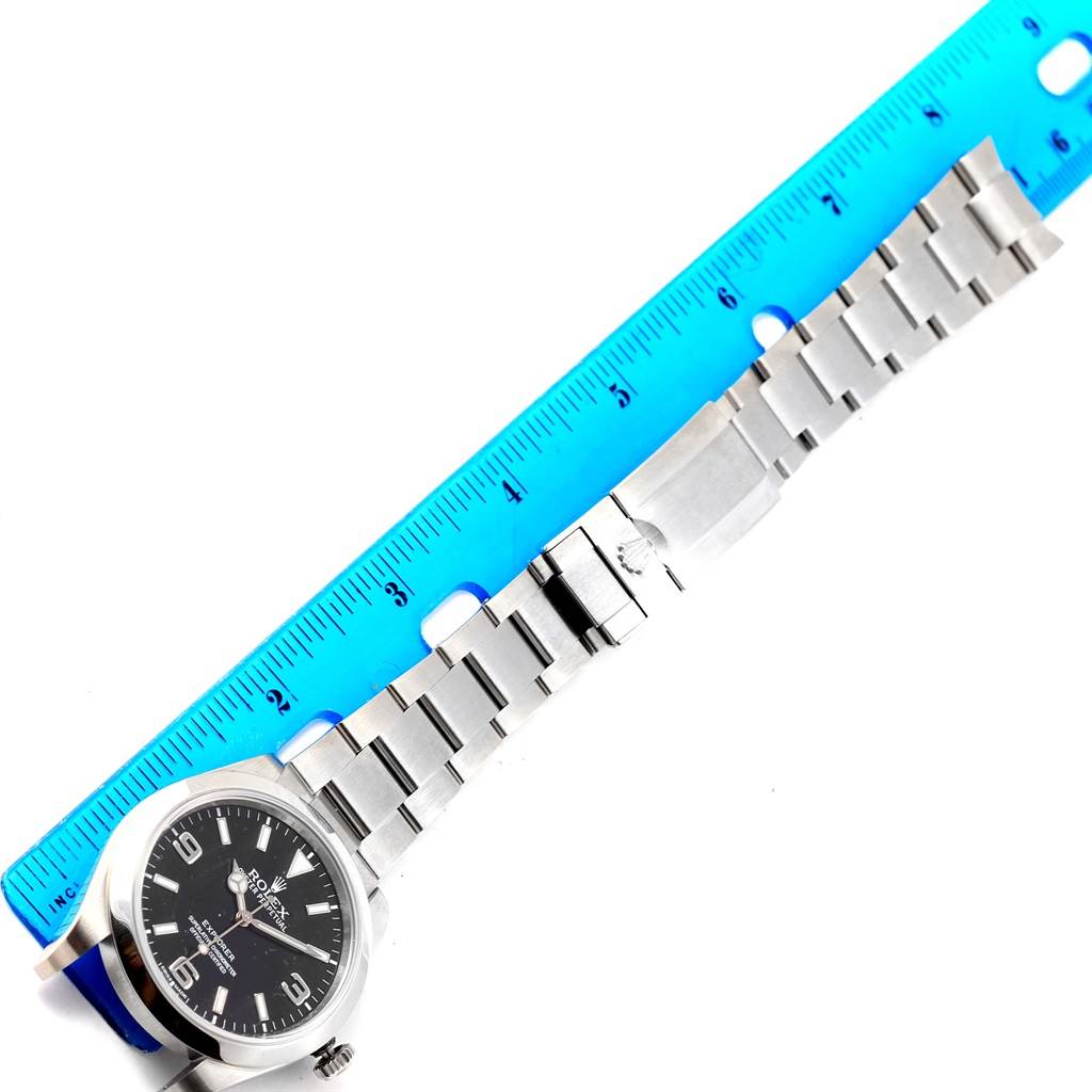 This image shows the Rolex Explorer 214270 Men's Stainless Steel Black Dial 214270 Men's Stainless Steel Black Dial watch laid out flat next to a blue ruler, displaying the watch face and metal bracelet.