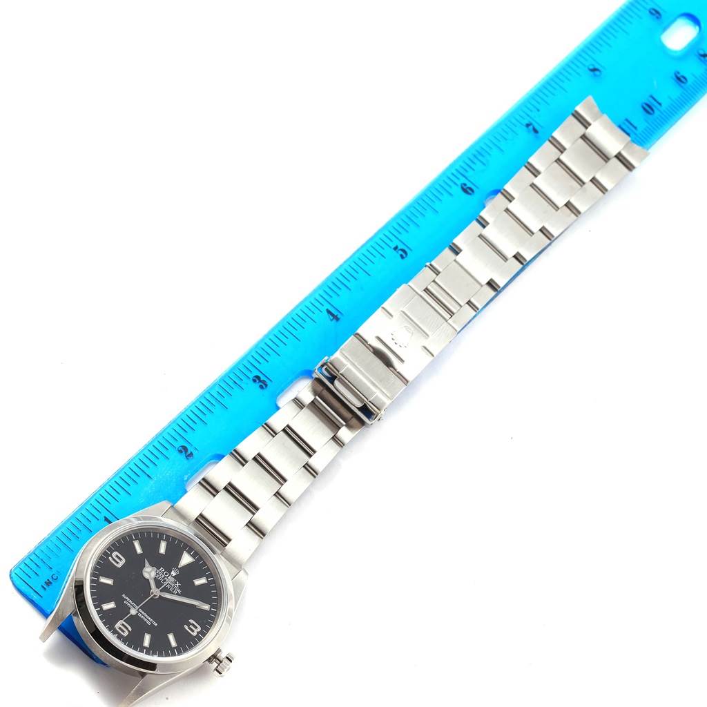 This image shows a Rolex Explorer 114270 Men's Stainless Steel Black Dial 114270 Men's Stainless Steel Black Dial model watch laid out flat, next to a ruler, displaying its face and bracelet clasp.