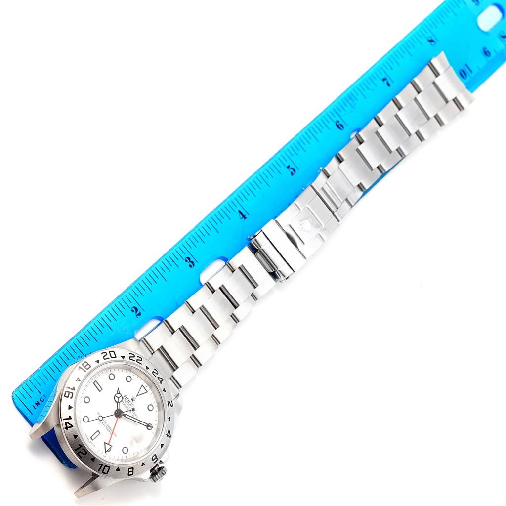 The image shows a Rolex Explorer 16570 Men's Stainless Steel White Dial 16570 Men's Stainless Steel White Dial watch, lying flat with a blue ruler alongside, displaying its face, bezel, bracelet, and clasp.