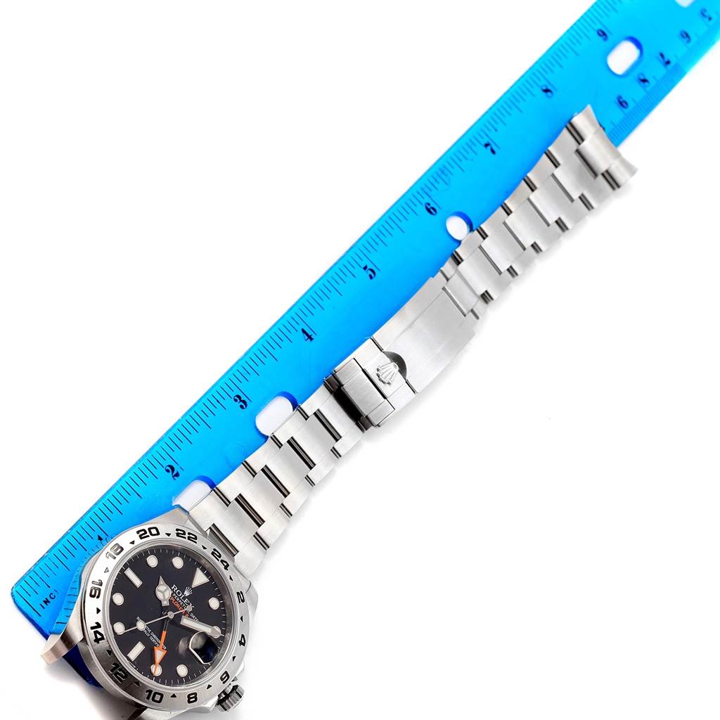 The Rolex Explorer 216570 Men's Stainless Steel Black Dial 216570 Men's Stainless Steel Black Dial watch is shown from a top-down angle, with its face, bracelet, and clasp alongside a blue ruler.