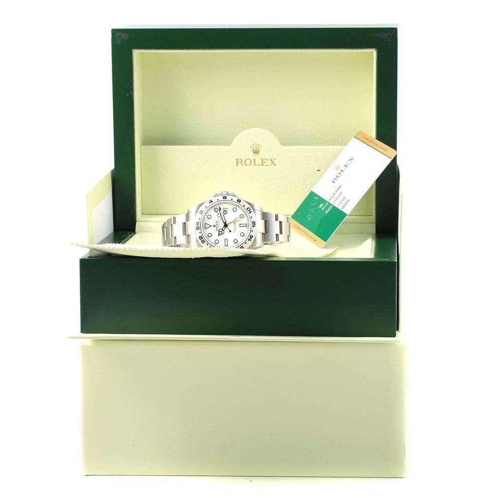 The Rolex Explorer 216570 Men's Stainless Steel White Dial 216570 Men's Stainless Steel White Dial watch is displayed at a slightly elevated angle in its open green box, with a warranty card on the right.