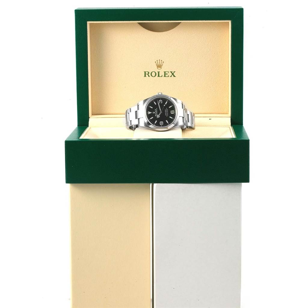 The watch pictured is a Rolex Explorer 214270 Men's Stainless Steel Black Dial 214270 Men's Stainless Steel Black Dial model displayed front-facing in its open green and beige box.
