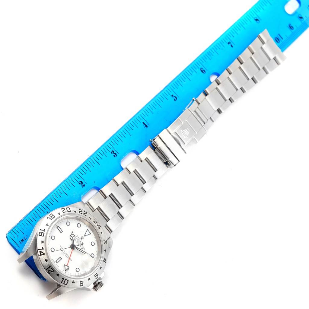 The image shows a Rolex Explorer 16570 Men's Stainless Steel White Dial 16570 Men's Stainless Steel White Dial watch laid flat alongside a blue ruler, showcasing its bracelet and clasp.