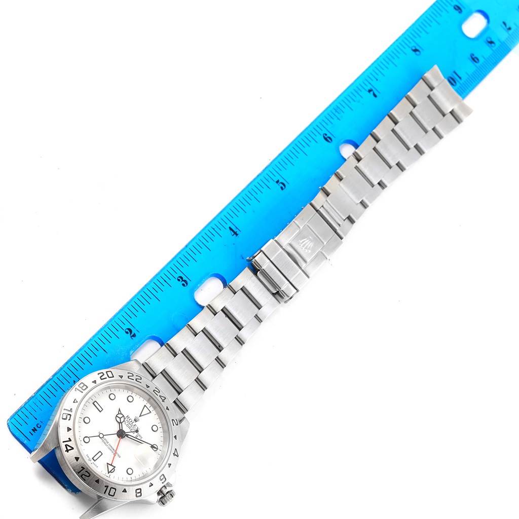 The Rolex Explorer 16570 Men's Stainless Steel White Dial 16570 Men's Stainless Steel White Dial watch is shown from a top-down angle, displaying the face, bezel, and bracelet alongside a blue ruler.