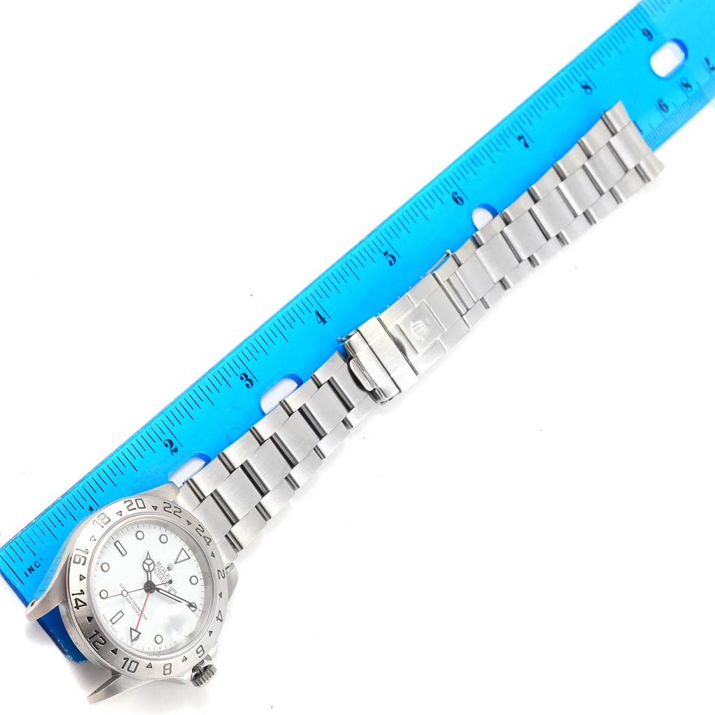 This image shows a Rolex Explorer 16570 Men's Stainless Steel White Dial 16570 Men's Stainless Steel White Dial watch laid flat alongside a blue ruler, highlighting the face and stainless steel bracelet.