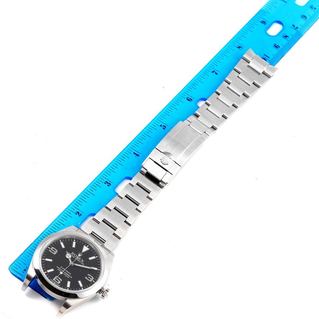 The image shows a Rolex Explorer 214270 Men's Stainless Steel Black Dial 214270 Men's Stainless Steel Black Dial watch laid flat with a blue ruler measuring its stainless steel bracelet.