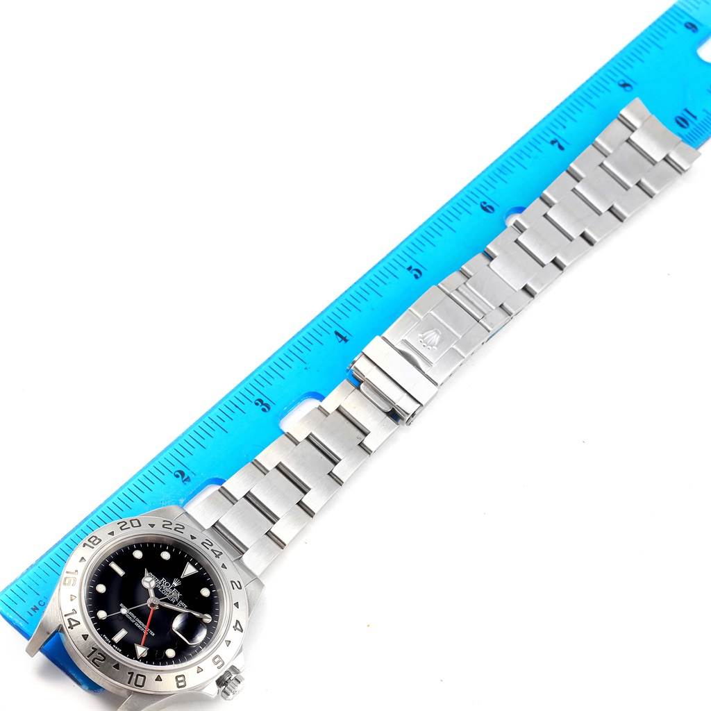 The image shows a horizontal view of a Rolex Explorer 16570 Men's Stainless Steel Black Dial 16570 Men's Stainless Steel Black Dial watch with its metal bracelet laid flat next to a blue ruler.