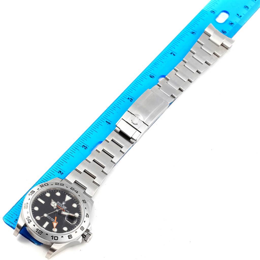 The Rolex Explorer 216570 Men's Stainless Steel Black Dial 216570 Men's Stainless Steel Black Dial watch is shown from above with the entire bracelet and clasp, alongside a blue ruler for scale.