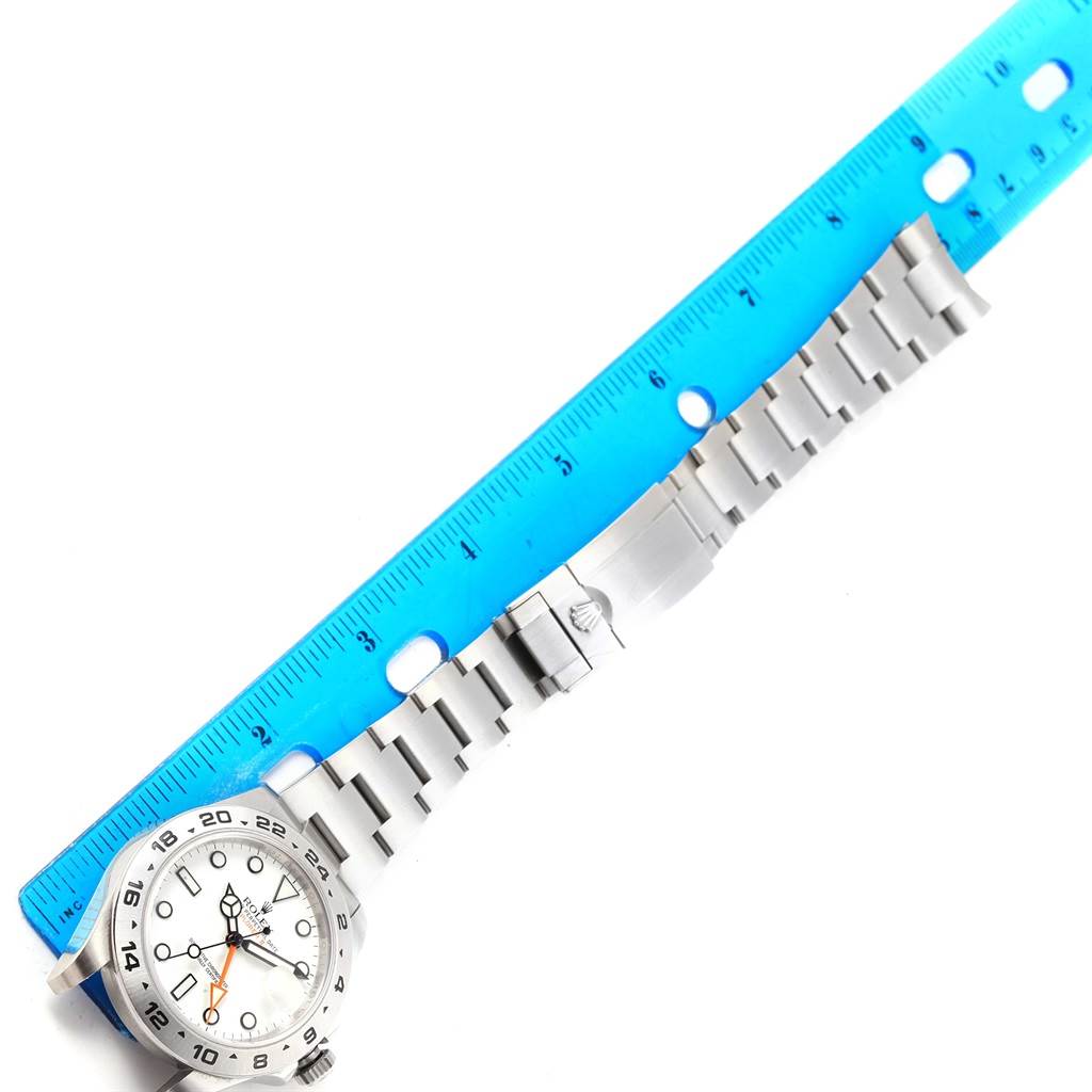This image shows a Rolex Explorer 216570 Men's Stainless Steel White Dial 216570 Men's Stainless Steel White Dial watch laid flat with a blue ruler alongside it for scale.