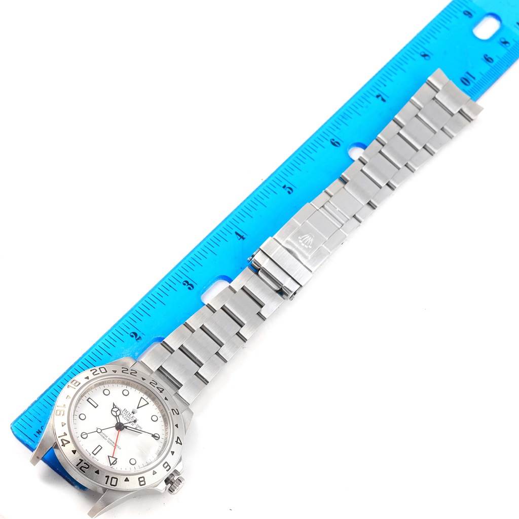 The Rolex Explorer 16570 Men's Stainless Steel White Dial 16570 Men's Stainless Steel White Dial watch is shown flat, with its face, bezel, crown, and bracelet visible alongside a blue ruler for scale.