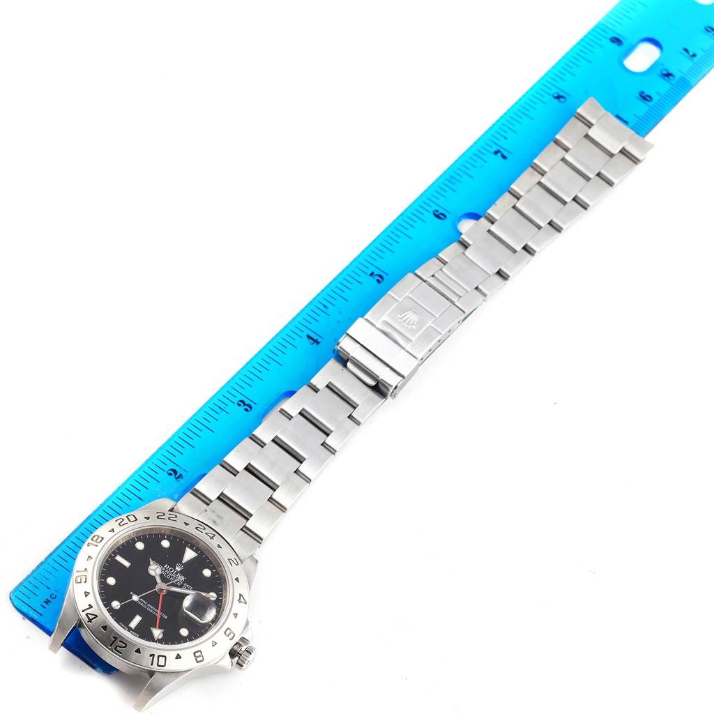 The Rolex Explorer 16570 Men's Stainless Steel Black Dial 16570 Men's Stainless Steel Black Dial watch is shown laid flat with its stainless steel bracelet extended alongside a blue ruler.