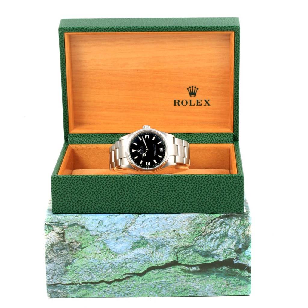 The Rolex Explorer 114270 Men's Stainless Steel Black Dial 114270 Men's Stainless Steel Black Dial watch is displayed front-facing inside an open green and tan presentation box.