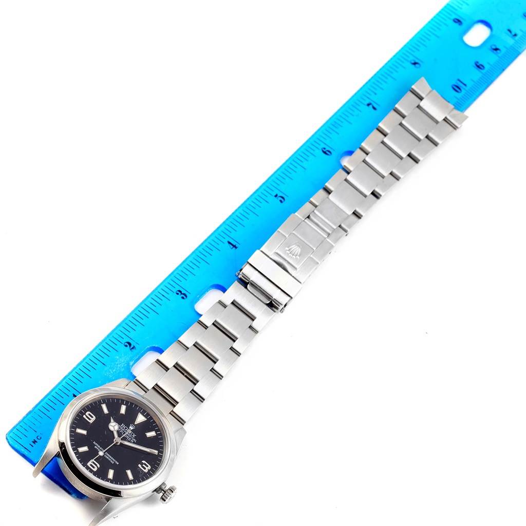 The image shows a top-down view of a Rolex Explorer 114270 Men's Stainless Steel Black Dial 114270 Men's Stainless Steel Black Dial watch placed next to a blue ruler for scale.