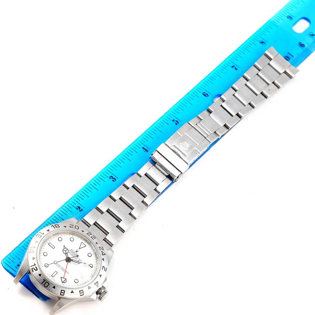The image shows a top-down view of a Rolex Explorer 16570 Men's Stainless Steel White Dial 16570 Men's Stainless Steel White Dial watch with its bracelet laid next to a blue ruler.