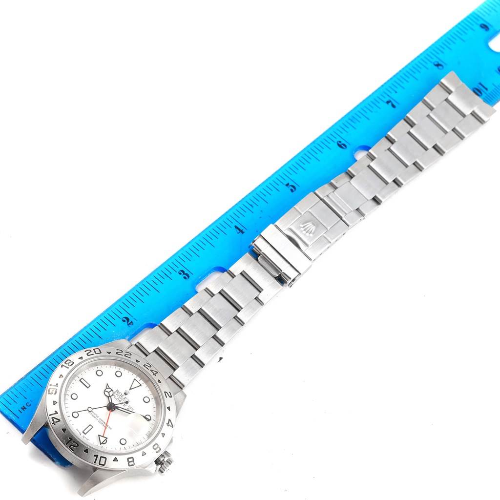 The image shows a full flat-lay view of a Rolex Explorer 16570 Men's Stainless Steel White Dial 16570 Men's Stainless Steel White Dial model, including the band, clasp, and dial alongside a blue ruler.