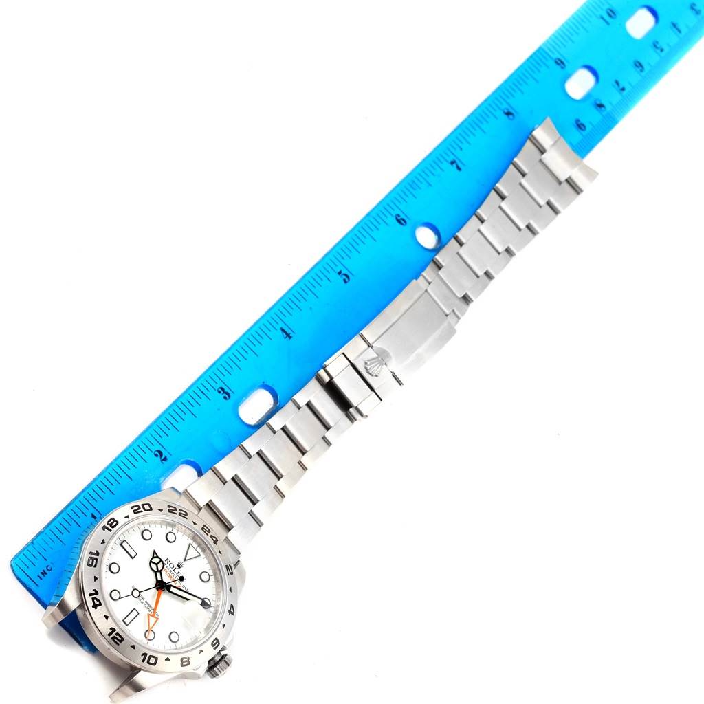 The image shows a top-down view of a Rolex Explorer 216570 Men's Stainless Steel White Dial 216570 Men's Stainless Steel White Dial watch, including its face and metal bracelet, with a blue ruler beside it.