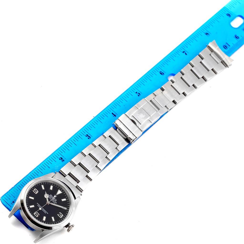 The image shows a Rolex Explorer 14270 Men's Stainless Steel Black Dial 14270 Men's Stainless Steel Black Dial watch placed next to a blue ruler, exhibiting the full length of the band and the watch face.