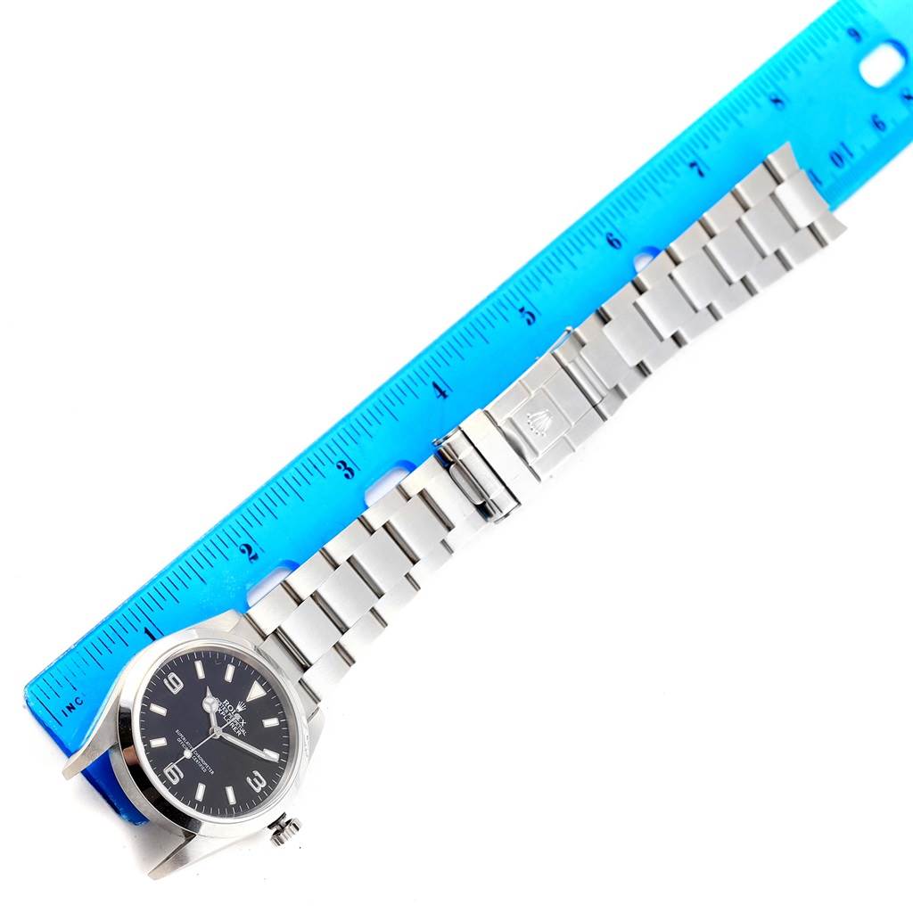 The image shows a Rolex Explorer 114270 Men's Stainless Steel Black Dial 114270 Men's Stainless Steel Black Dial watch laid flat against a blue ruler, displaying the dial, casing, and metal bracelet.