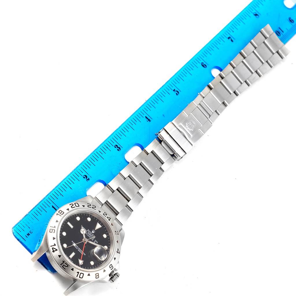 The Rolex Explorer 16570 Men's Stainless Steel Black Dial 16570 Men's Stainless Steel Black Dial watch is shown with its dial and entire bracelet band extended next to a blue ruler.