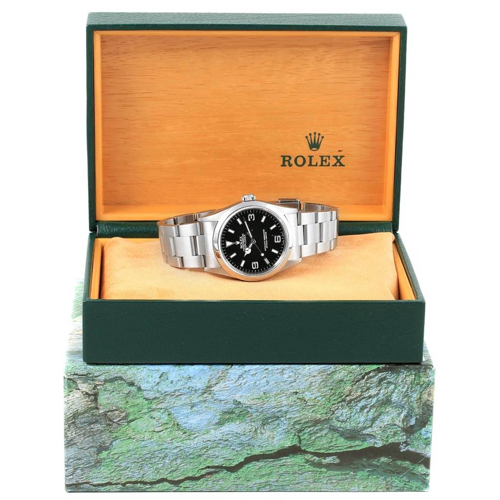 The Rolex Explorer 14270 Men's Stainless Steel Black Dial 14270 Men's Stainless Steel Black Dial watch is shown from the front inside its green and yellow box with the bracelet and dial in view.
