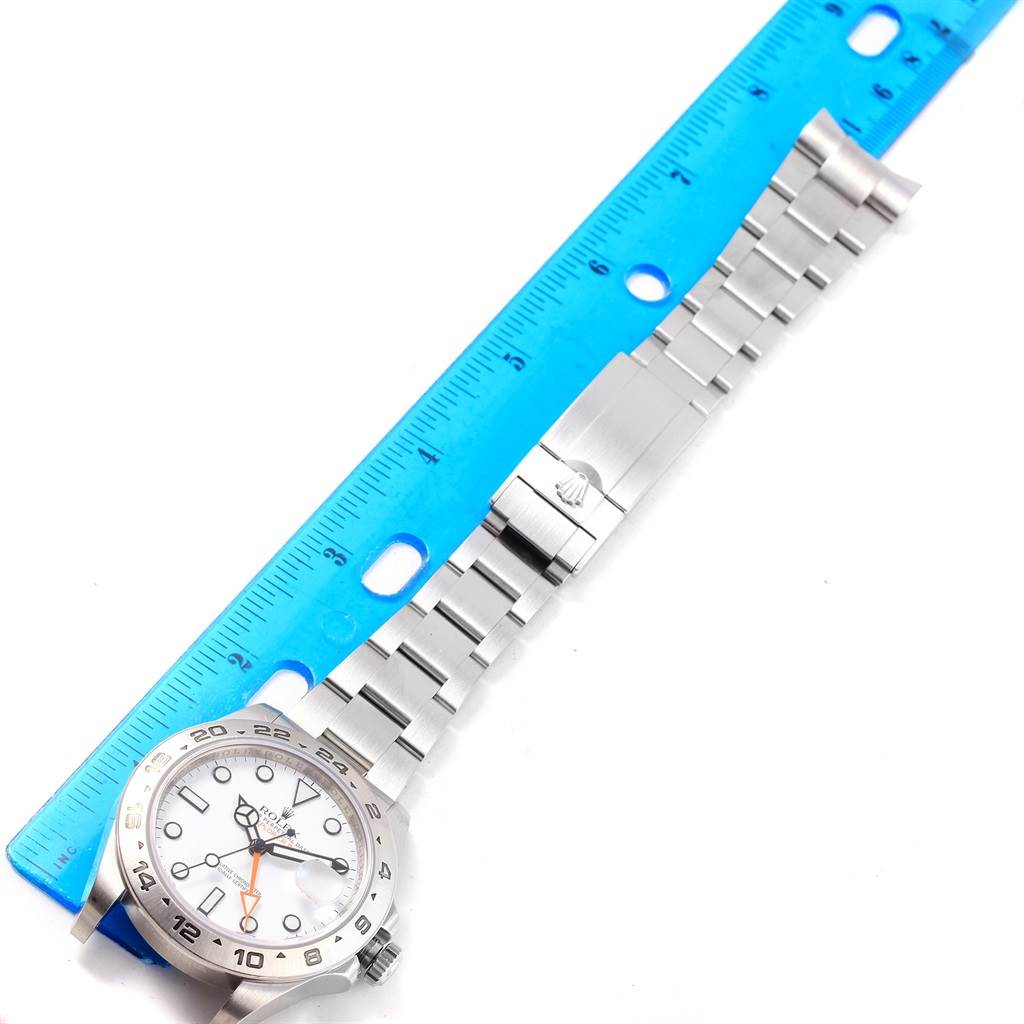 The image shows a side view of a Rolex Explorer 216570 Men's Stainless Steel White Dial 216570 Men's Stainless Steel White Dial watch with its bracelet extended next to a blue ruler.
