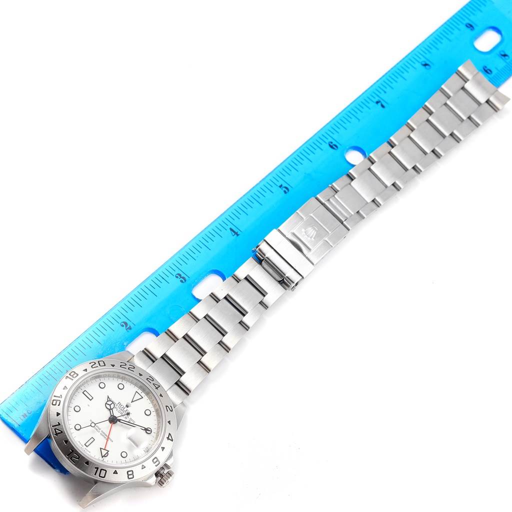 The image shows a Rolex Explorer 16570 Men's Stainless Steel White Dial 16570 Men's Stainless Steel White Dial watch laid flat next to a ruler, displaying its strap and face from a top-down angle.