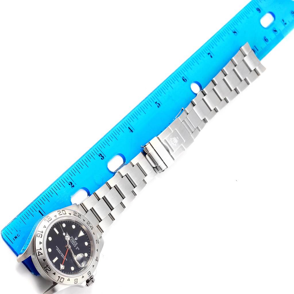 This image shows a Rolex Explorer 16570 Men's Stainless Steel Black Dial 16570 Men's Stainless Steel Black Dial watch laid flat with its band extended next to a blue ruler.