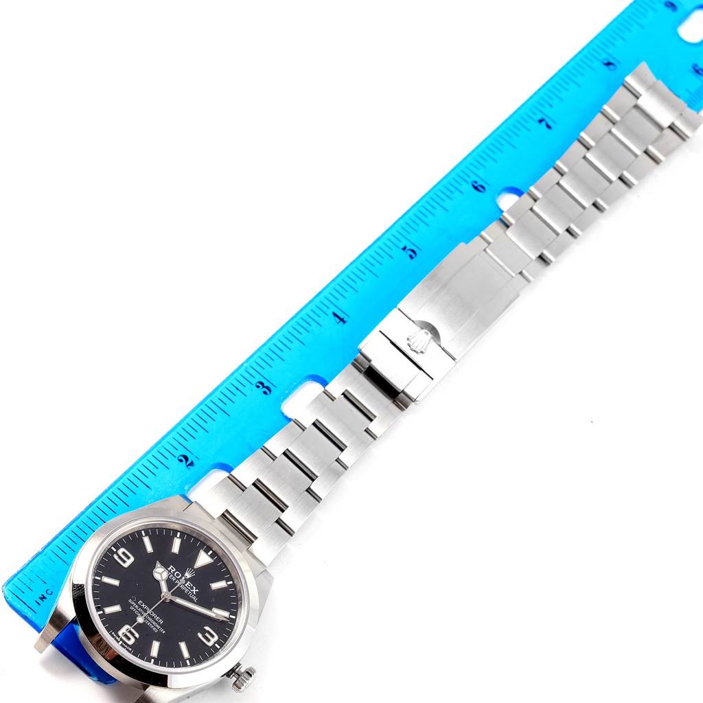 The image shows a Rolex Explorer 214270 Men's Stainless Steel Black Dial 214270 Men's Stainless Steel Black Dial watch laid flat next to a ruler, highlighting the watch face and bracelet.