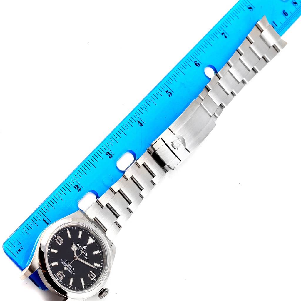 The image shows a Rolex Explorer 214270 Men's Stainless Steel Black Dial 214270 Men's Stainless Steel Black Dial watch laid flat next to a ruler, displaying its face and bracelet.