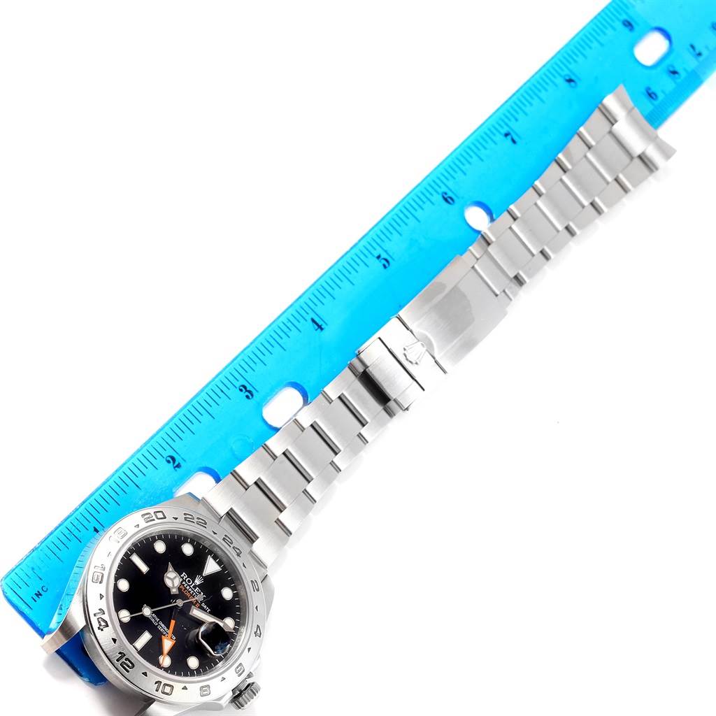 The image shows a Rolex Explorer 216570 Men's Stainless Steel Black Dial 216570 Men's Stainless Steel Black Dial watch, face up, placed next to a blue ruler to measure its bracelet.