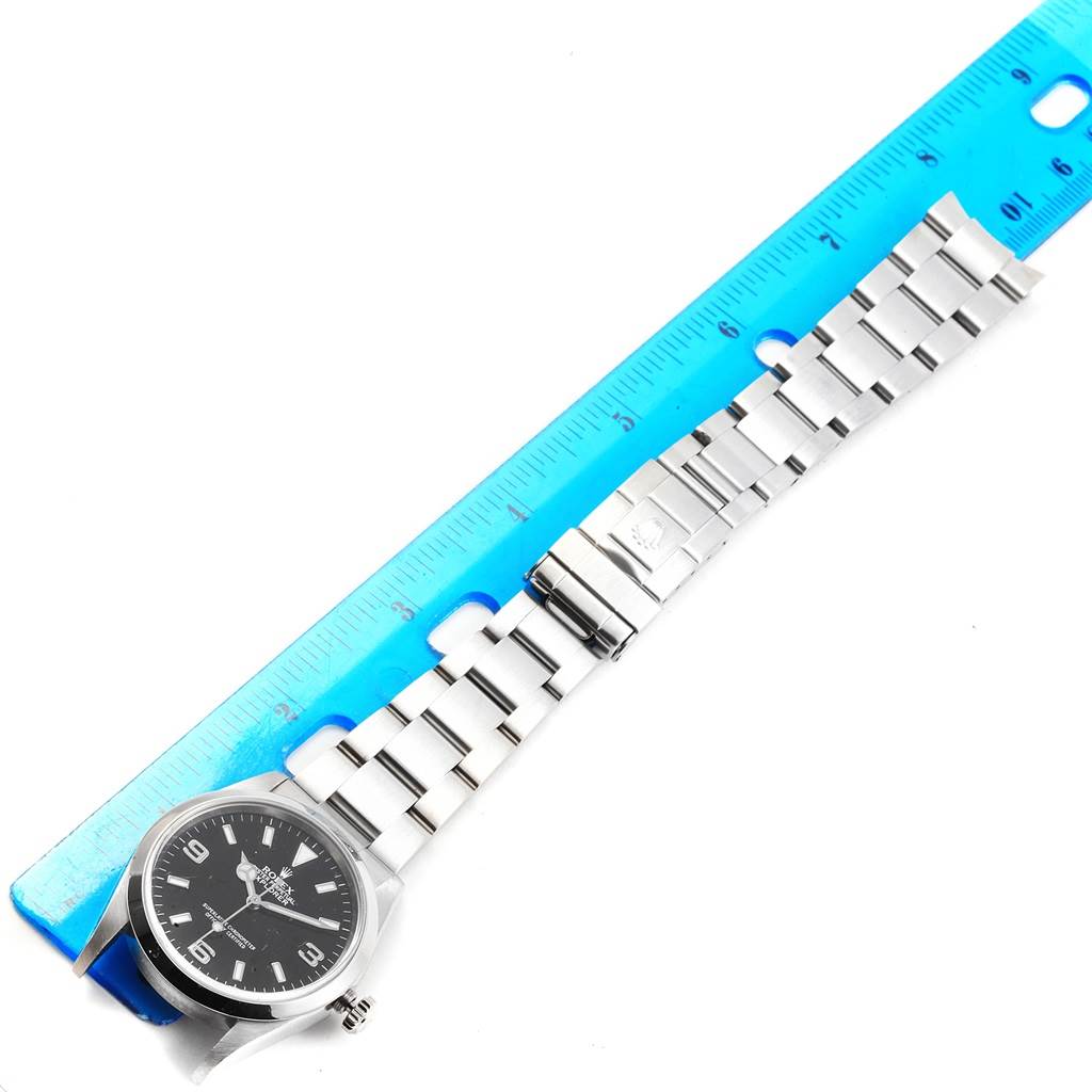 The Rolex Explorer 114270 Men's Stainless Steel Black Dial 114270 Men's Stainless Steel Black Dial watch is shown from an overhead angle, including the face, bracelet, and clasp, accompanied by a ruler.