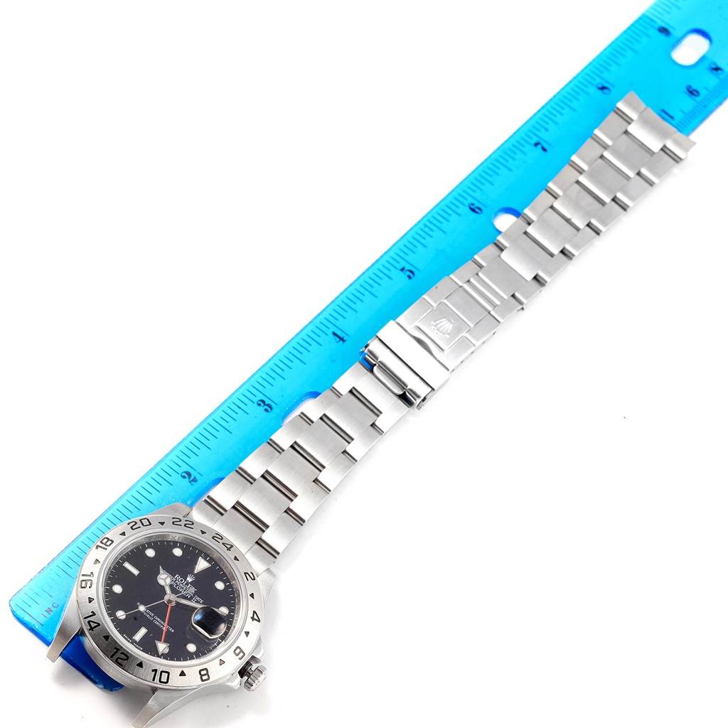 The Rolex Explorer 16570 Men's Stainless Steel Black Dial 16570 Men's Stainless Steel Black Dial watch is shown from a top-down angle, displaying the dial, bezel, bracelet, and clasp next to a ruler.