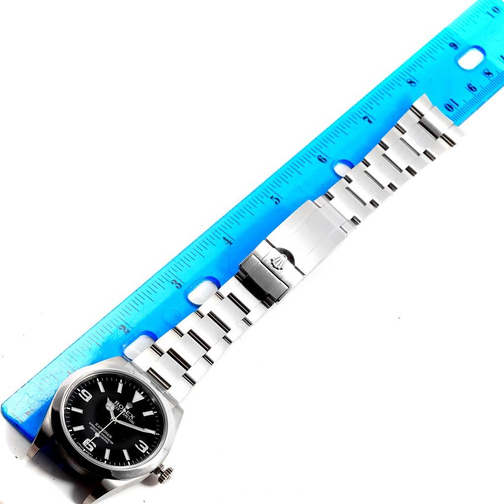 The image shows a top-down view of a Rolex Explorer 214270 Men's Stainless Steel Black Dial 214270 Men's Stainless Steel Black Dial watch with a blue ruler measuring the bracelet.