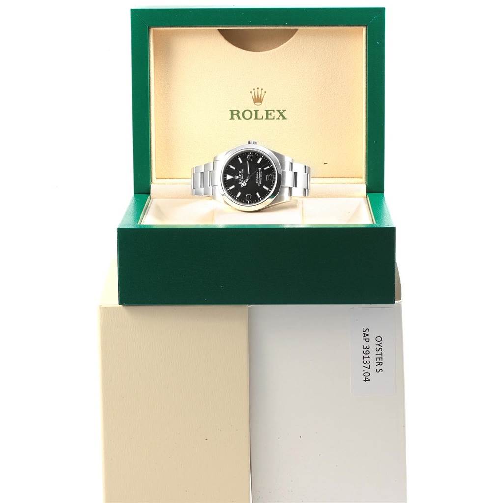 The Rolex Explorer 214270 Men's Stainless Steel Black Dial 214270 Men's Stainless Steel Black Dial watch is displayed from a front angle within its green and beige Rolex box.