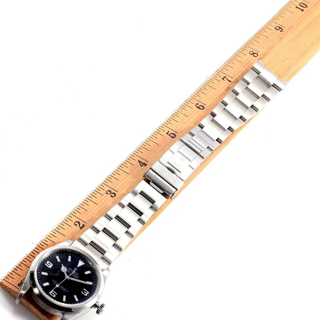 The image shows a Rolex Explorer 114270 Men's Stainless Steel Black Dial 114270 Men's Stainless Steel Black Dial watch, including its face and metal bracelet, placed alongside a measuring ruler.