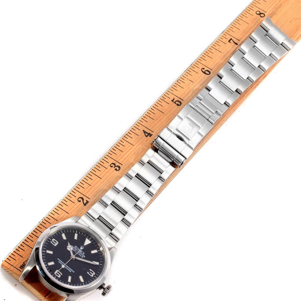 The image shows a Rolex Explorer 114270 Men's Stainless Steel Black Dial 114270 Men's Stainless Steel Black Dial watch laid flat on a ruler, displaying its face, bezel, and stainless steel bracelet.