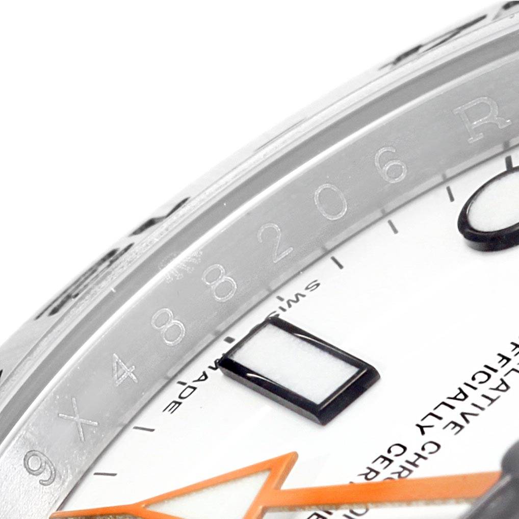 This close-up angle of the Rolex Explorer 216570 Men's Stainless Steel White Dial 216570 Men's Stainless Steel White Dial watch shows part of the bezel, dial, and triangular orange second hand.