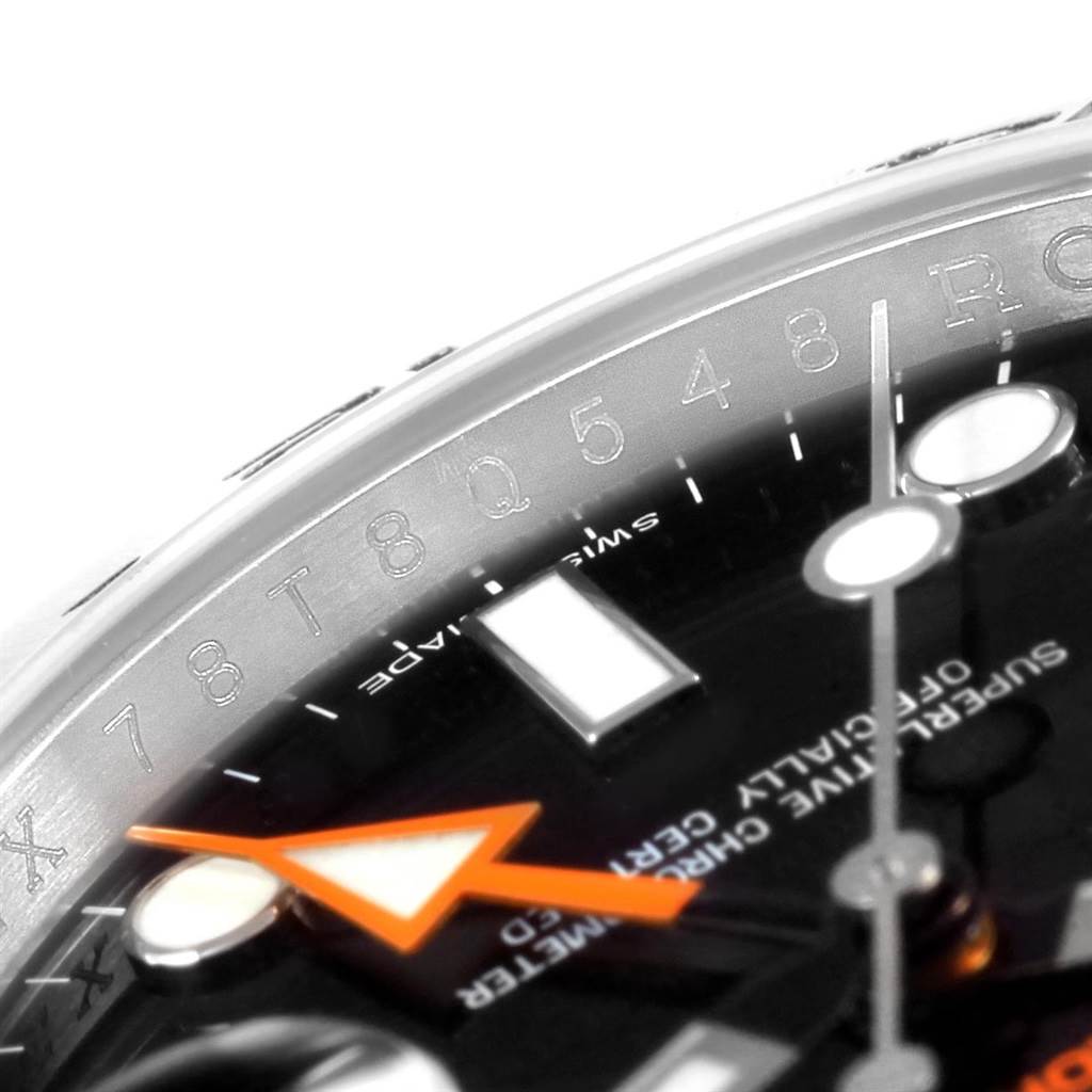 This close-up angle of the Rolex Explorer 216570 Men's Stainless Steel Black Dial 216570 Men's Stainless Steel Black Dial watch shows the dial with an orange hand, indices, and part of the bezel engraved with numbers.
