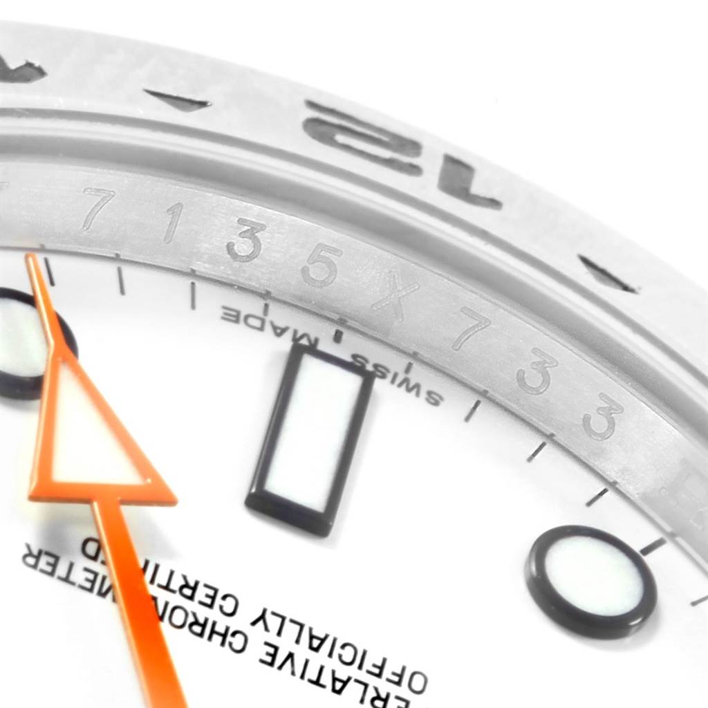 This close-up image of the Rolex Explorer 216570 Men's Stainless Steel White Dial 216570 Men's Stainless Steel White Dial watch shows the bezel, partial dial, and hour marker with an orange hand.