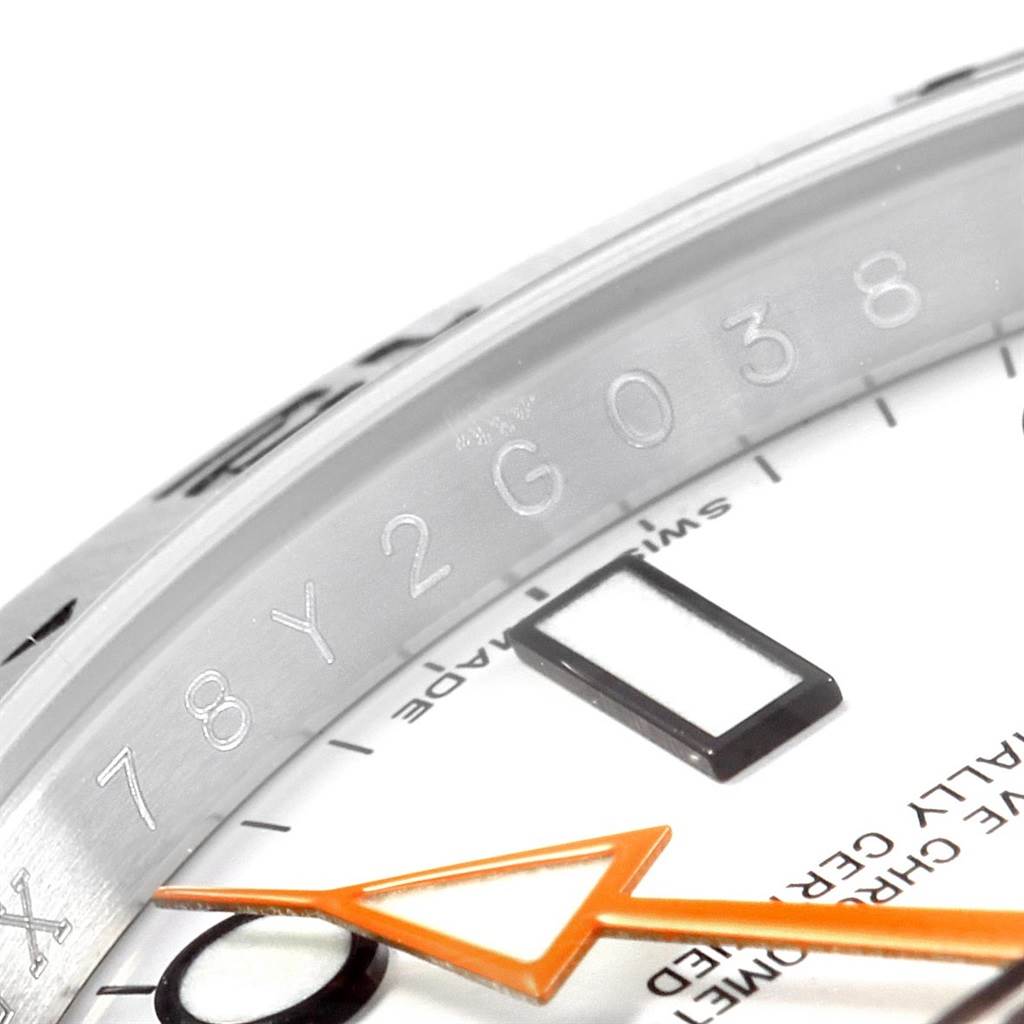 This close-up image of the Rolex Explorer 216570 Men's Stainless Steel White Dial 216570 Men's Stainless Steel White Dial shows the engraved bezel and part of the face with the orange arrow hand.