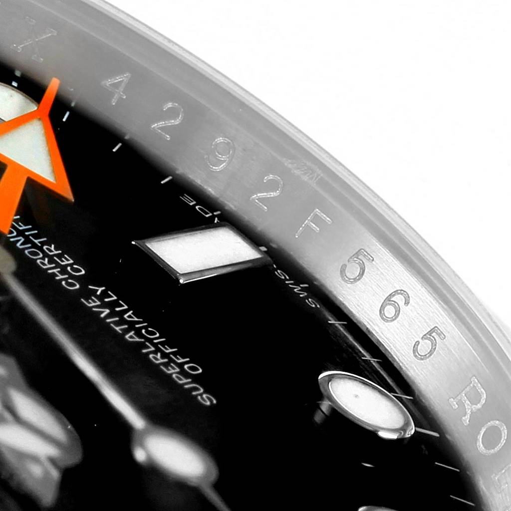 This close-up of the Rolex Explorer 216570 Men's Stainless Steel Black Dial 216570 Men's Stainless Steel Black Dial watch shows part of the dial and bezel, featuring the minute markings and an orange hand.