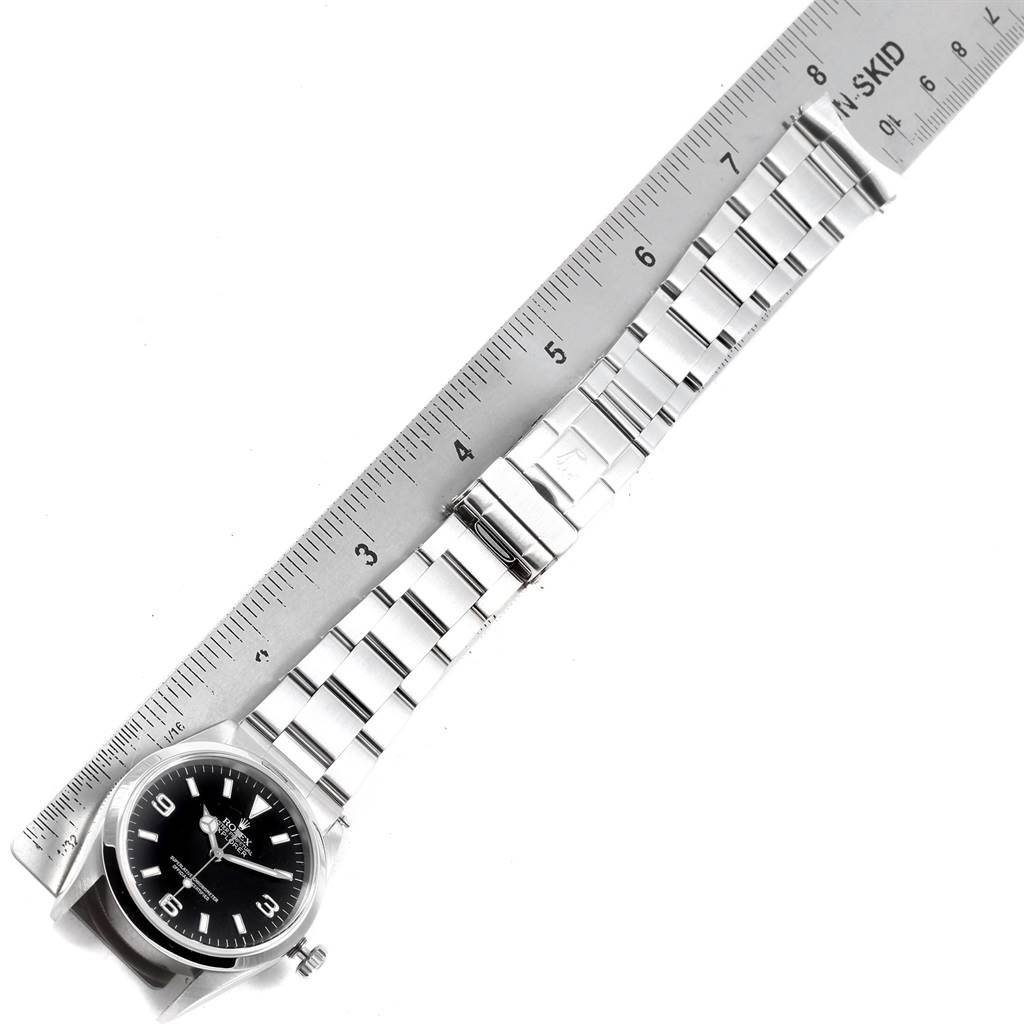 The Rolex Explorer 14270 Men
s Stainless Steel Black Dial 14270 Men
s Stainless Steel Black Dial watch is shown from a top-down angle, displaying its black dial and metal band alongside a measuring ruler.