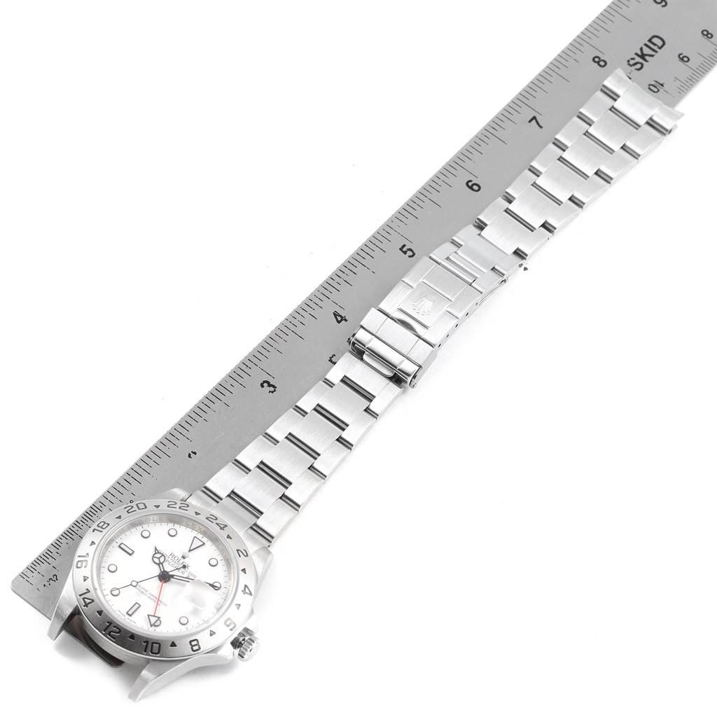 The Rolex Explorer 16570 Men
s Stainless Steel White Dial 16570 Men
s Stainless Steel White Dial watch is shown lying flat with a side view of the face and bracelet placed next to a ruler.